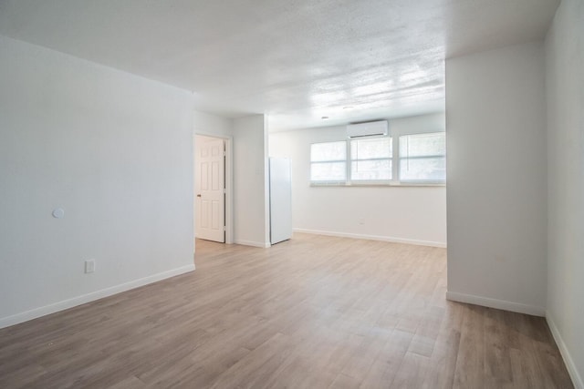 unfurnished room with a wall mounted AC and light hardwood / wood-style flooring