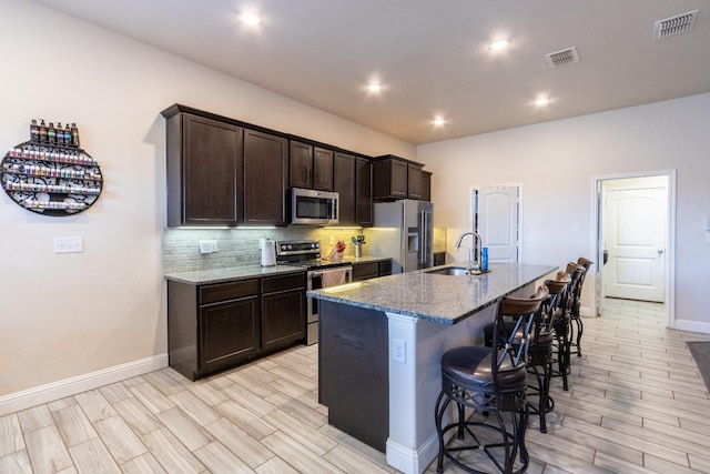 kitchen featuring appliances with stainless steel finishes, sink, decorative backsplash, dark stone counters, and a kitchen island with sink