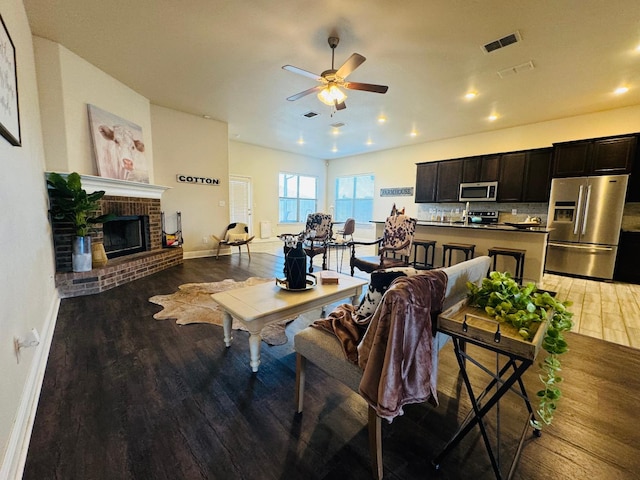 living room featuring hardwood / wood-style flooring, ceiling fan, and a brick fireplace