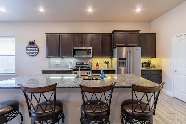 kitchen with stainless steel appliances, light stone countertops, a breakfast bar area, and a center island with sink