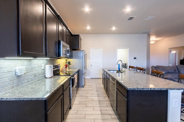 kitchen with sink, a kitchen breakfast bar, a kitchen island with sink, light stone counters, and stainless steel appliances