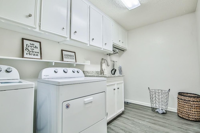 washroom with cabinets, a textured ceiling, washer and clothes dryer, and light hardwood / wood-style floors