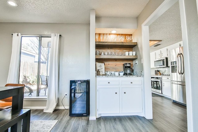 bar featuring hardwood / wood-style floors, stainless steel appliances, beverage cooler, and white cabinets