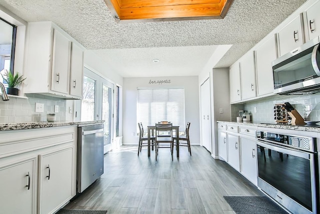 kitchen featuring appliances with stainless steel finishes, light stone countertops, light hardwood / wood-style floors, and white cabinets