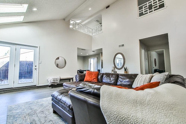 living room featuring a skylight, high vaulted ceiling, a textured ceiling, beam ceiling, and hardwood / wood-style floors