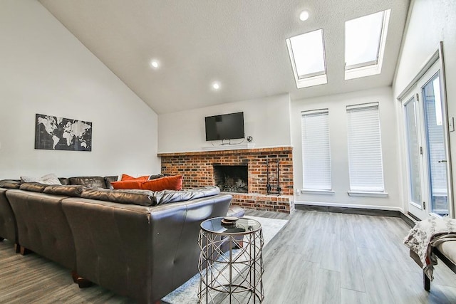 living room with wood-type flooring, vaulted ceiling with skylight, and a brick fireplace