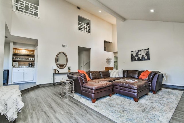 living room featuring hardwood / wood-style flooring, built in features, beamed ceiling, and a towering ceiling