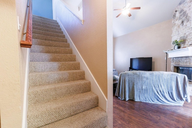 stairway featuring hardwood / wood-style floors, a stone fireplace, and ceiling fan