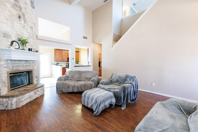 living room with dark hardwood / wood-style flooring, beam ceiling, a fireplace, and a high ceiling