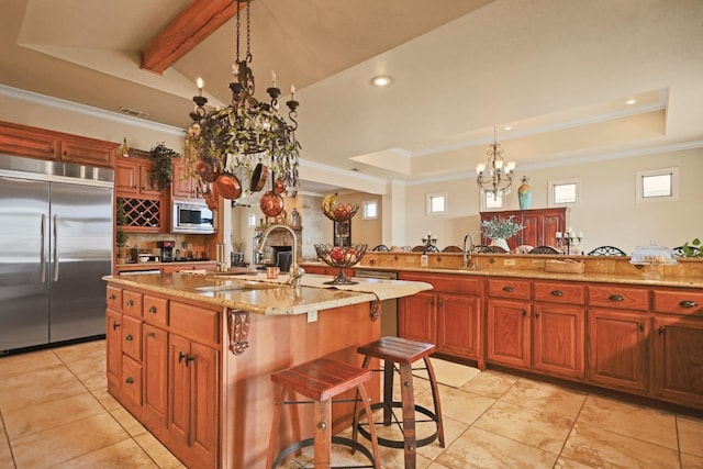 kitchen with a kitchen bar, sink, built in appliances, a center island with sink, and a tray ceiling