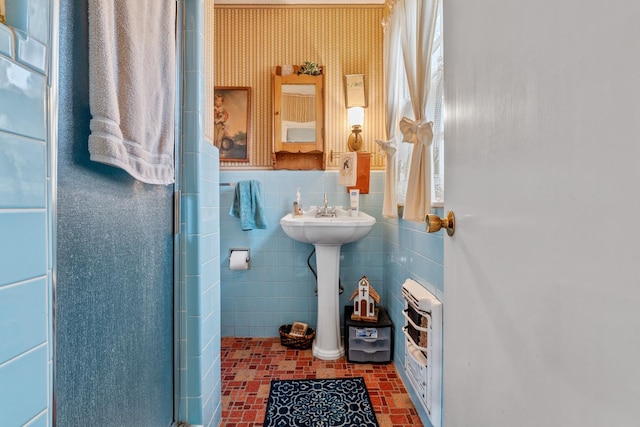 bathroom with heating unit, an enclosed shower, sink, and tile walls