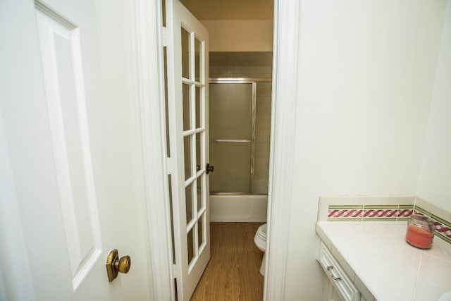 full bathroom with bath / shower combo with glass door, vanity, wood-type flooring, and toilet