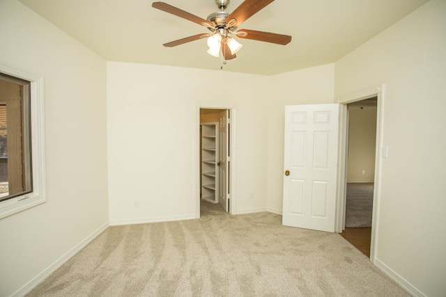 unfurnished bedroom featuring a walk in closet, light colored carpet, ceiling fan, and a closet