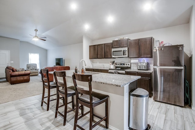 kitchen with sink, appliances with stainless steel finishes, a kitchen island with sink, a kitchen breakfast bar, and vaulted ceiling