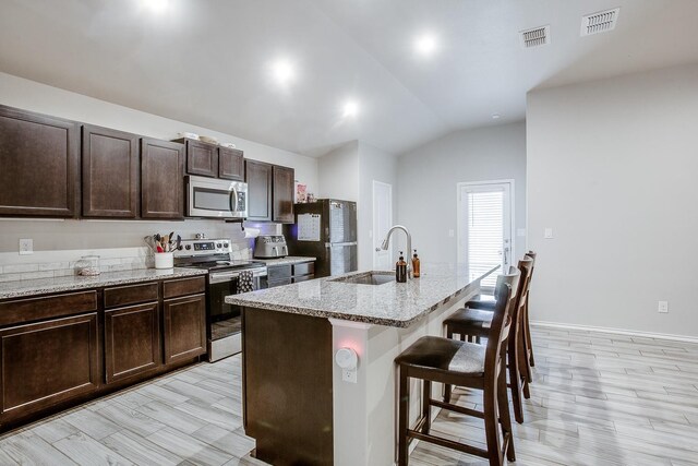 kitchen featuring sink, dark brown cabinets, stainless steel appliances, a center island with sink, and a kitchen bar