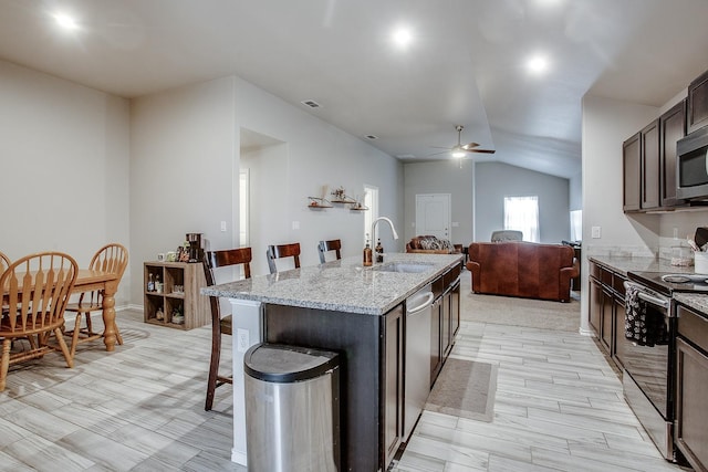 kitchen with dark brown cabinetry, sink, a center island with sink, appliances with stainless steel finishes, and a kitchen breakfast bar