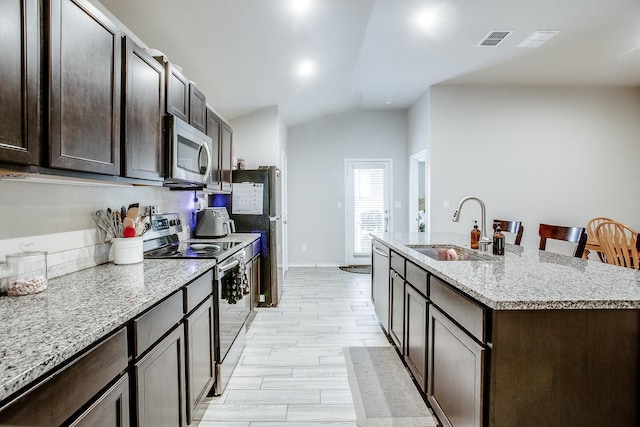 kitchen featuring lofted ceiling, sink, light stone counters, stainless steel appliances, and a kitchen island with sink