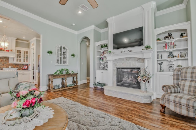 living room featuring built in shelves, ornamental molding, ceiling fan, and light wood-type flooring