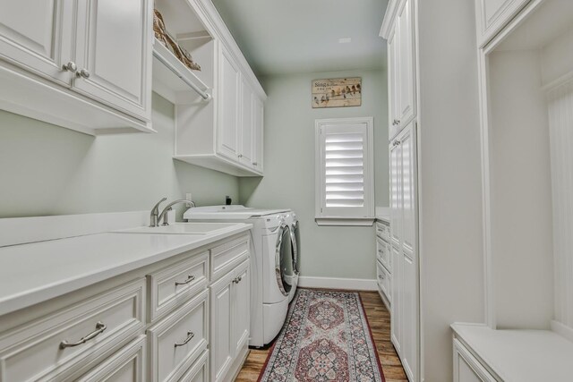 laundry area with independent washer and dryer, cabinets, sink, and hardwood / wood-style floors