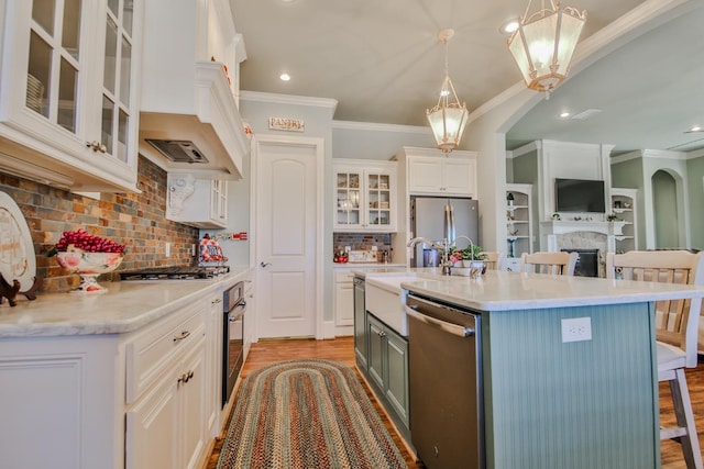 kitchen featuring a breakfast bar, decorative light fixtures, white cabinetry, stainless steel appliances, and a center island with sink