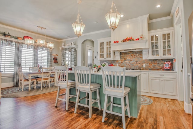 kitchen with white cabinetry, decorative backsplash, a center island with sink, decorative light fixtures, and light wood-type flooring