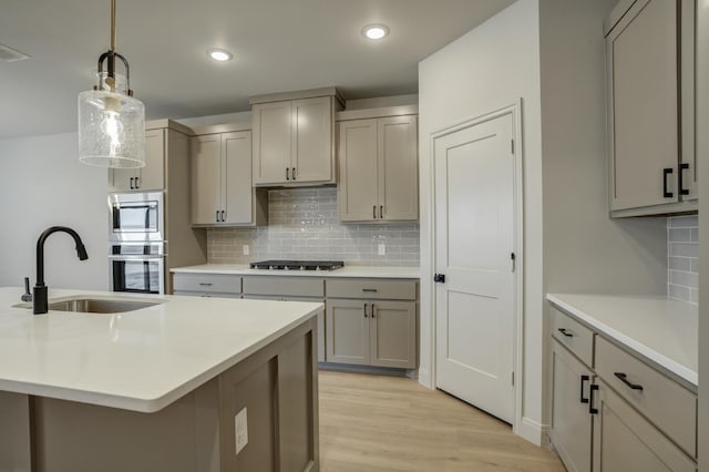 kitchen with gray cabinetry, sink, decorative light fixtures, and an island with sink