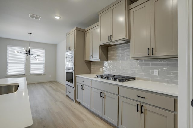 kitchen featuring pendant lighting, gray cabinets, backsplash, stainless steel appliances, and light hardwood / wood-style floors