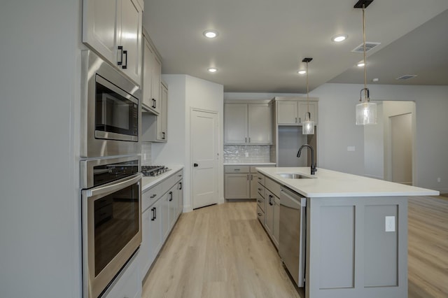 kitchen with sink, decorative light fixtures, light hardwood / wood-style flooring, appliances with stainless steel finishes, and an island with sink