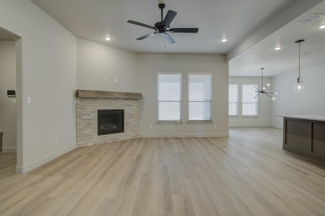 unfurnished living room with a fireplace, ceiling fan with notable chandelier, and light hardwood / wood-style flooring