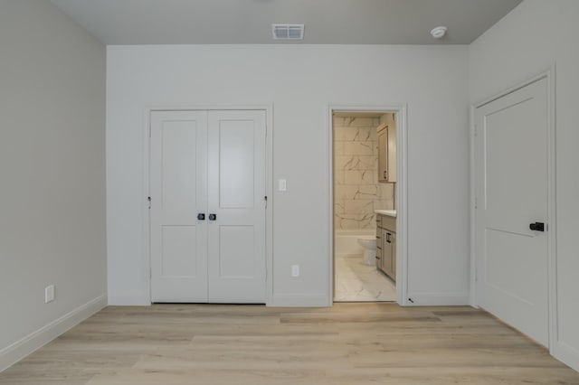 unfurnished bedroom with ensuite bathroom, light hardwood / wood-style floors, and a closet