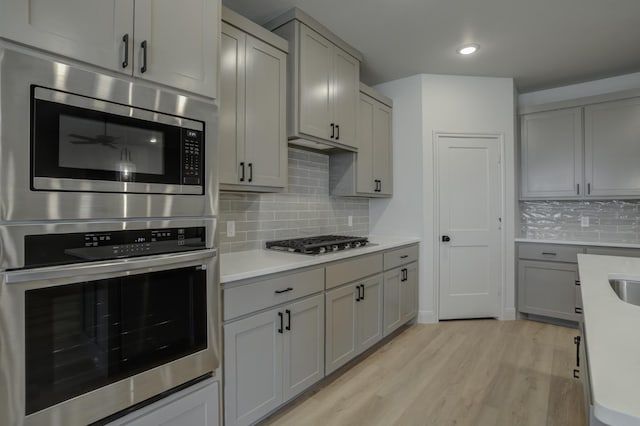 kitchen featuring tasteful backsplash, stainless steel appliances, light hardwood / wood-style floors, and gray cabinetry