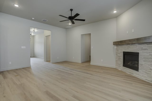 unfurnished living room featuring ceiling fan, a stone fireplace, and light hardwood / wood-style floors