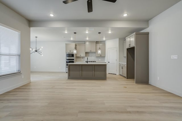 kitchen with a kitchen island with sink, hanging light fixtures, gray cabinetry, stainless steel microwave, and decorative backsplash