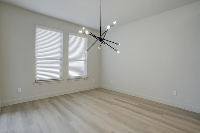 unfurnished room with a notable chandelier and light hardwood / wood-style floors