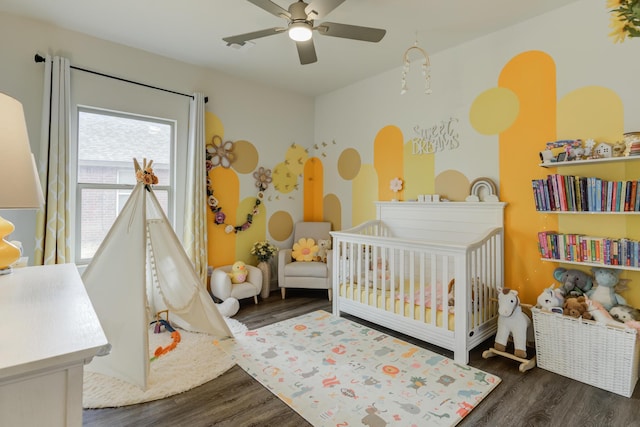 bedroom with a crib, wood finished floors, and a ceiling fan