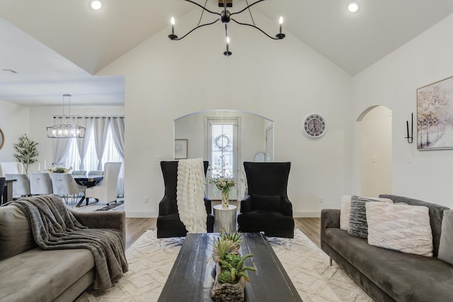 living area with light wood-type flooring, high vaulted ceiling, a notable chandelier, and arched walkways