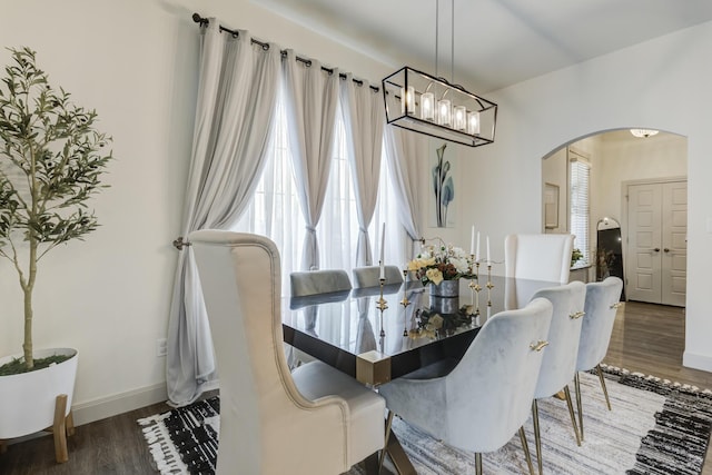 dining area with baseboards, arched walkways, an inviting chandelier, and wood finished floors