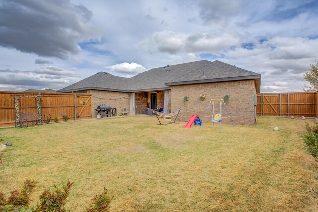 rear view of property with a yard, a shingled roof, brick siding, and a fenced backyard
