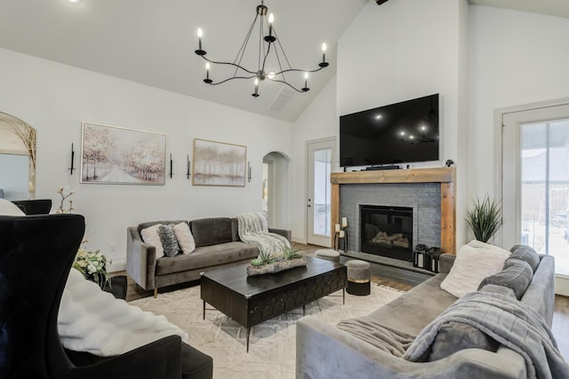 living area featuring arched walkways, an inviting chandelier, a glass covered fireplace, light wood-type flooring, and high vaulted ceiling