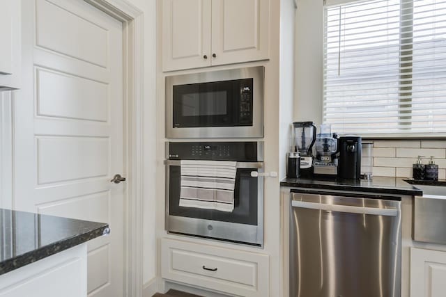 kitchen with dark stone countertops, white cabinets, appliances with stainless steel finishes, and plenty of natural light