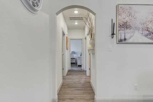 corridor featuring arched walkways, visible vents, wood finished floors, and baseboards