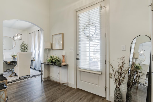 entryway with arched walkways, a notable chandelier, baseboards, and dark wood-type flooring