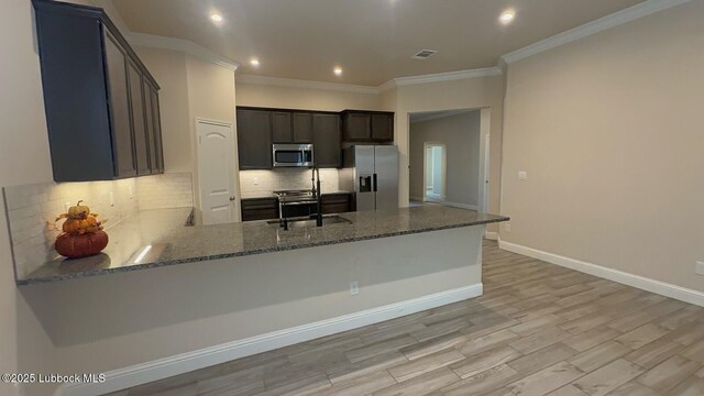 7501 100th St, Lubbock, TX 79424 - kitchen featuring stainless steel appliances, dark stone counters, ornamental molding, decorative backsplash, and a peninsula