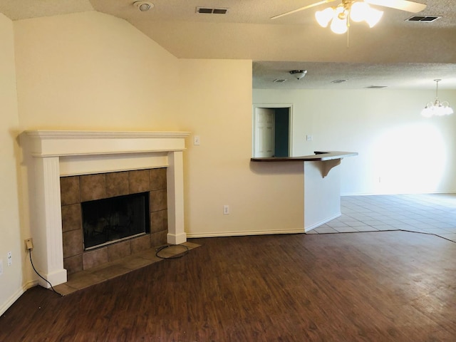 unfurnished living room with lofted ceiling, hardwood / wood-style flooring, a fireplace, a textured ceiling, and ceiling fan with notable chandelier