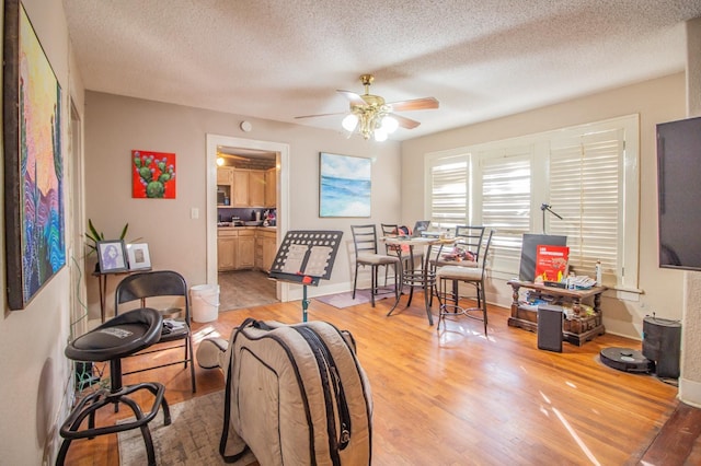 living room with ceiling fan, a textured ceiling, and light hardwood / wood-style floors