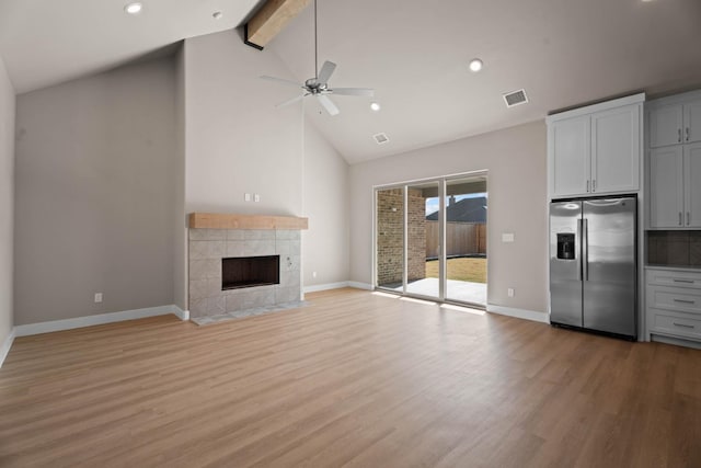 unfurnished living room featuring beam ceiling, high vaulted ceiling, a tile fireplace, and light hardwood / wood-style flooring