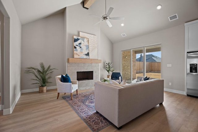 living room featuring high vaulted ceiling, a tiled fireplace, ceiling fan, beam ceiling, and light hardwood / wood-style flooring