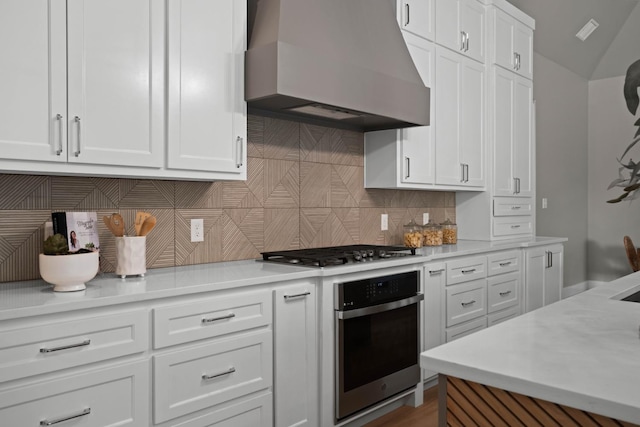 kitchen featuring white cabinetry, backsplash, premium range hood, and appliances with stainless steel finishes