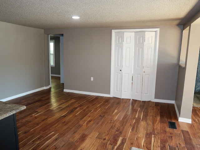 unfurnished bedroom with a textured ceiling, dark hardwood / wood-style flooring, and a closet