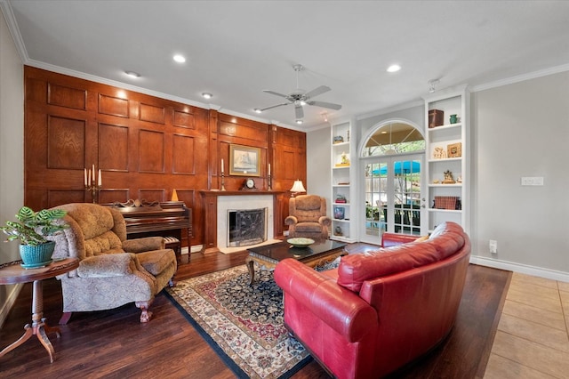 living room with built in shelves, french doors, wood-type flooring, ornamental molding, and ceiling fan